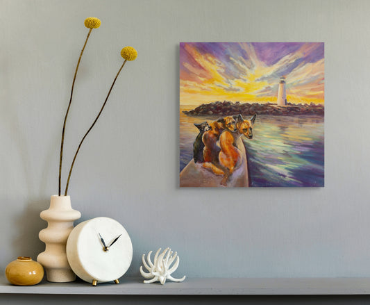 Interior mockup with the painting Paddle Pals hanging on a light gray wall above a shelf with modern decor, showing dogs on a paddleboard at sunset near Walton Lighthouse in Santa Cruz.