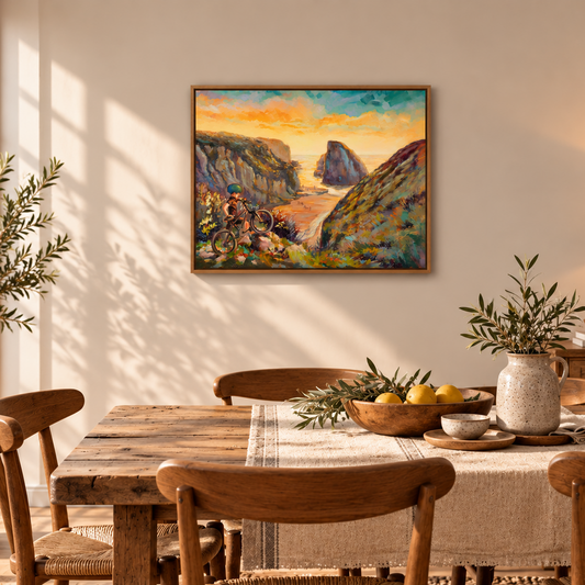 Wild and Earned coastal adventure art print by Martina Goulart, featuring a young cyclist overlooking a rocky beach at sunset, displayed in a warm, rustic dining room with natural wood furniture and soft sunlight.