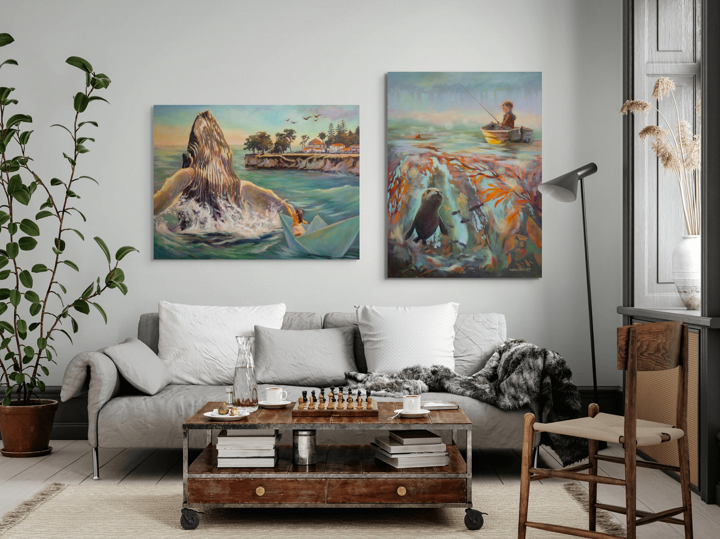 Two large coastal paintings hanging above a sofa: one of a girl in a paper boat beside a breaching whale, and the other of a boy fishing above a kelp forest with a seal.
