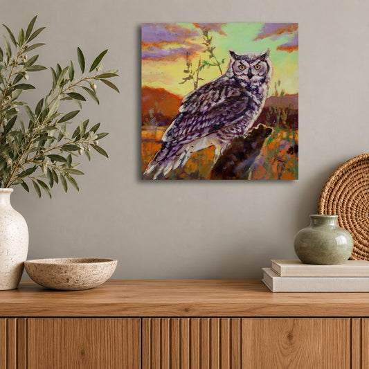 Original wildlife oil painting of a great horned owl perched on a branch against a colorful sunset sky by Martina Goulart, displayed in a modern living room with natural wood furnishings.