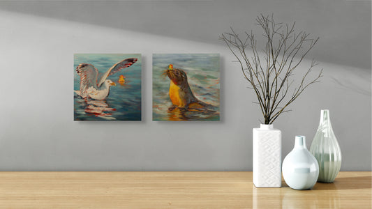 Two Wild Neighbors paintings — seal and seagull — hanging above a table with three white vases and a twig, coastal wildlife art by Martina Goulart.
