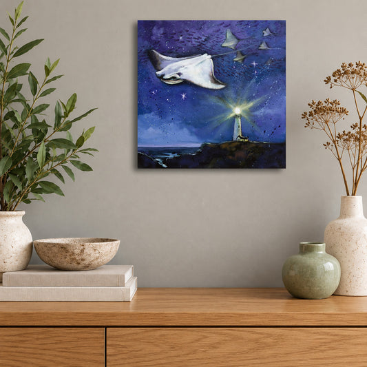 Original oil painting by Martina Goulart featuring graceful manta rays flying through a star-filled night sky above a glowing coastal lighthouse, displayed on a neutral wall above a wooden cabinet.