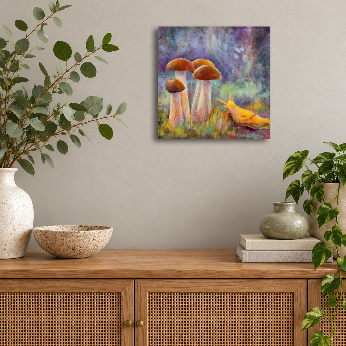 Colorful original oil painting by Martina Goulart featuring four woodland mushrooms and a bright yellow banana slug in a whimsical forest scene, displayed above a wooden cabinet in a modern living room.