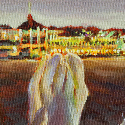 Seal’s flipper and tail in the foreground with the Santa Cruz Beach Boardwalk glowing in colorful nighttime lights behind it, reflecting on the water.