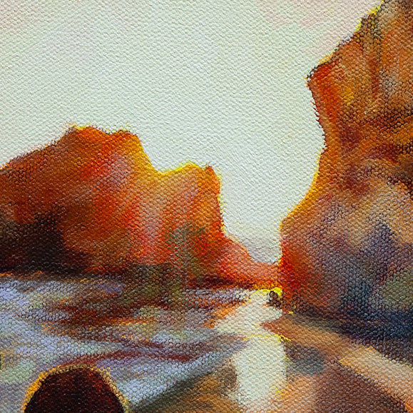 Detail of glowing sunset light between coastal rock formations along the shoreline.
