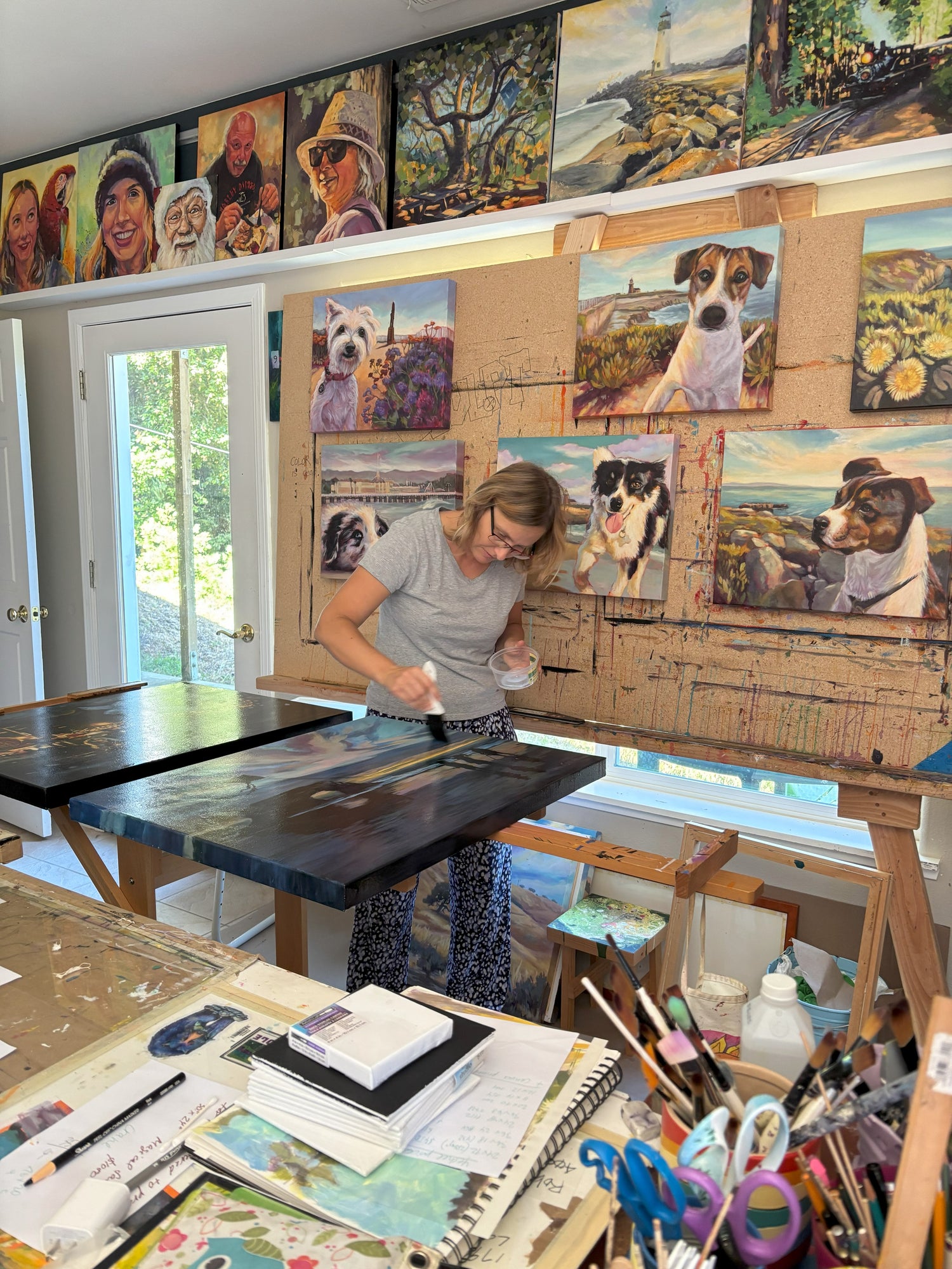Artist Martina Goulart working on paintings in her Santa Cruz Mountains studio, surrounded by colorful original artwork.