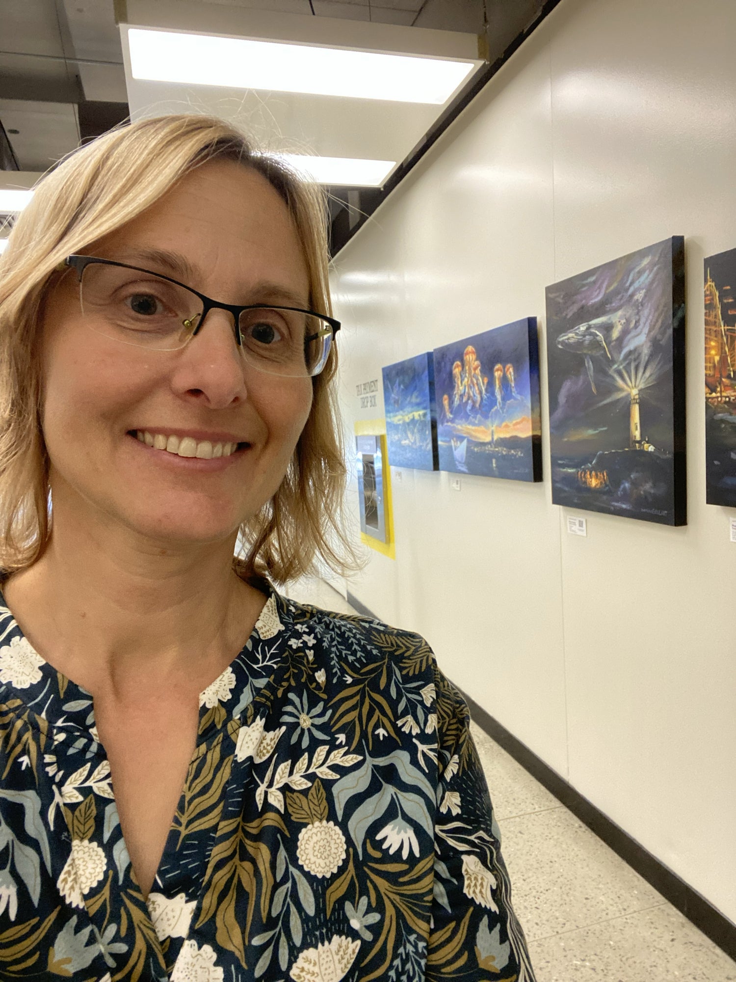 Woman with glasses standing in a hallway with art on the wall
