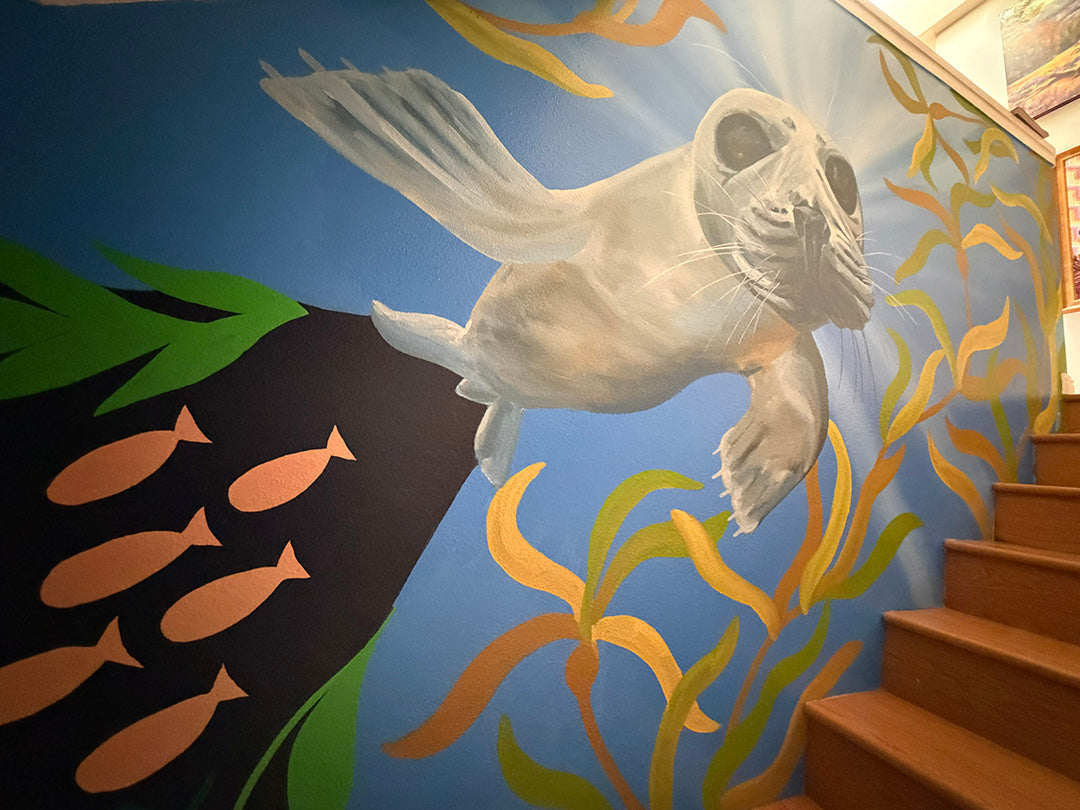 A colorful mural painted on a staircase wall featuring a white seal swimming underwater with orange fish and yellow-green seaweed on a blue background.
