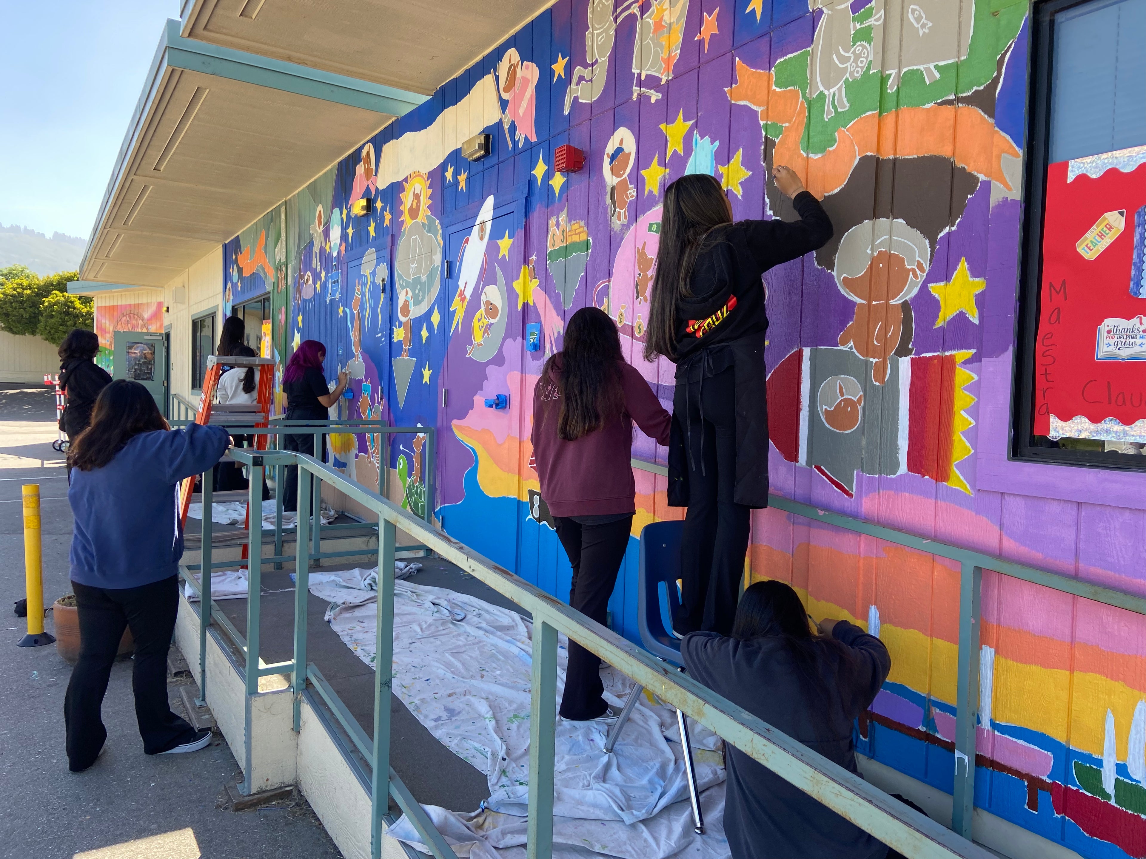 Group of people painting a colorful mural on the side of a building.