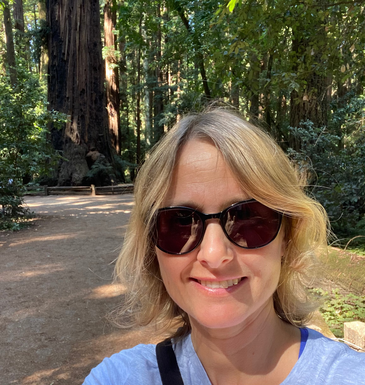 Woman wearing sunglasses and a blue shirt in a forest setting