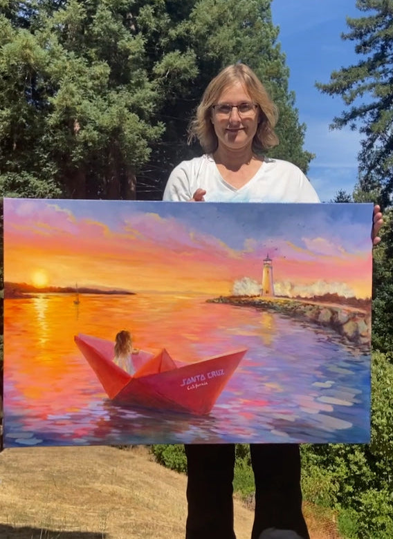 Woman holding a painting of a woman in a red boat at sunset with a lighthouse.