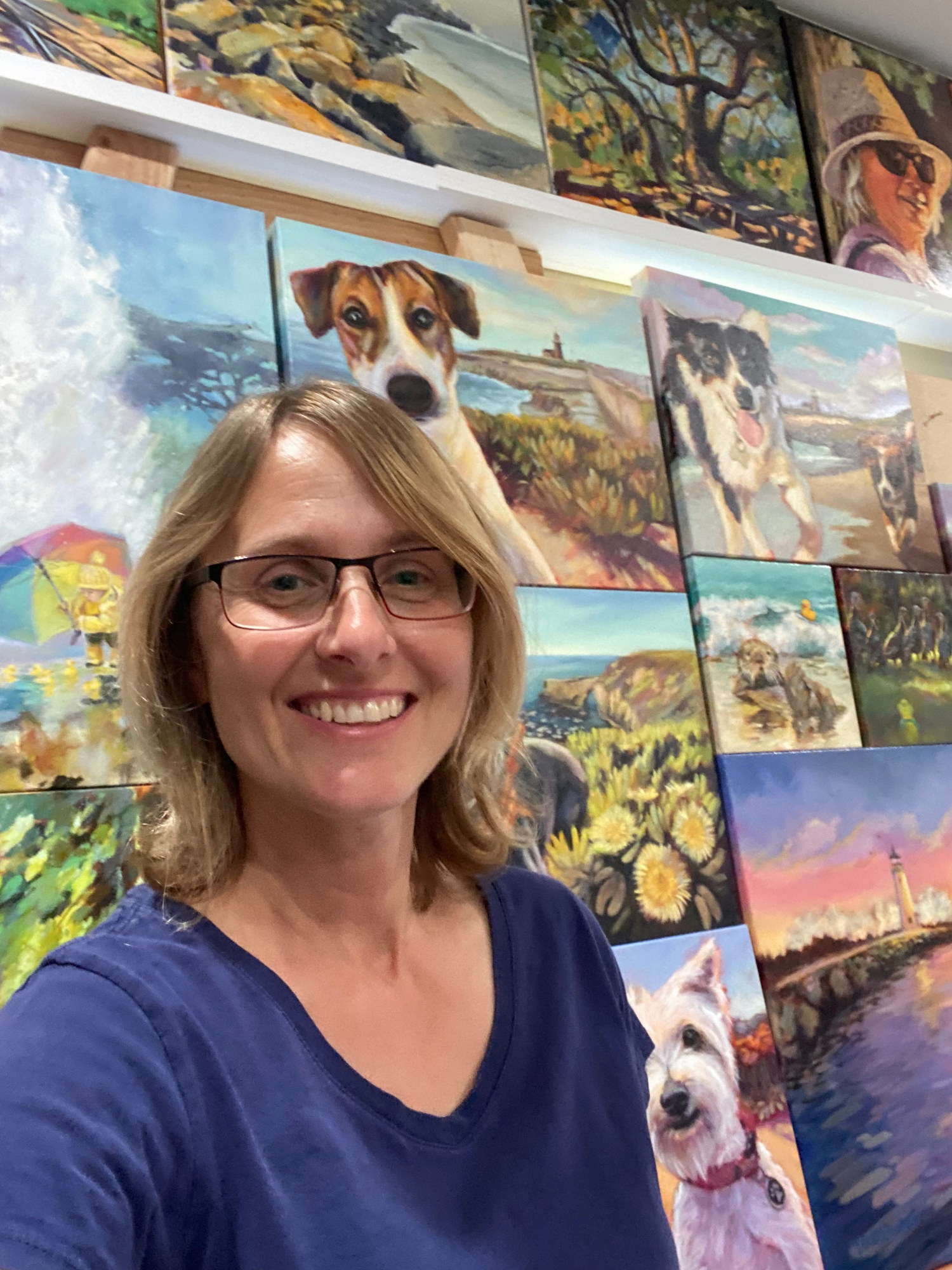 Woman in a blue shirt smiling and standing in front of a wall of dog paintings