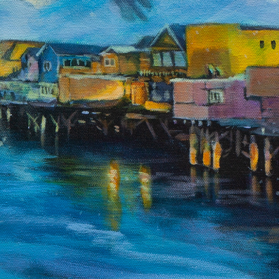 Close-up of Monterey pier buildings — pink, yellow, and blue — with shining lights and reflections in teal-blue water from Echoes of Monterey.