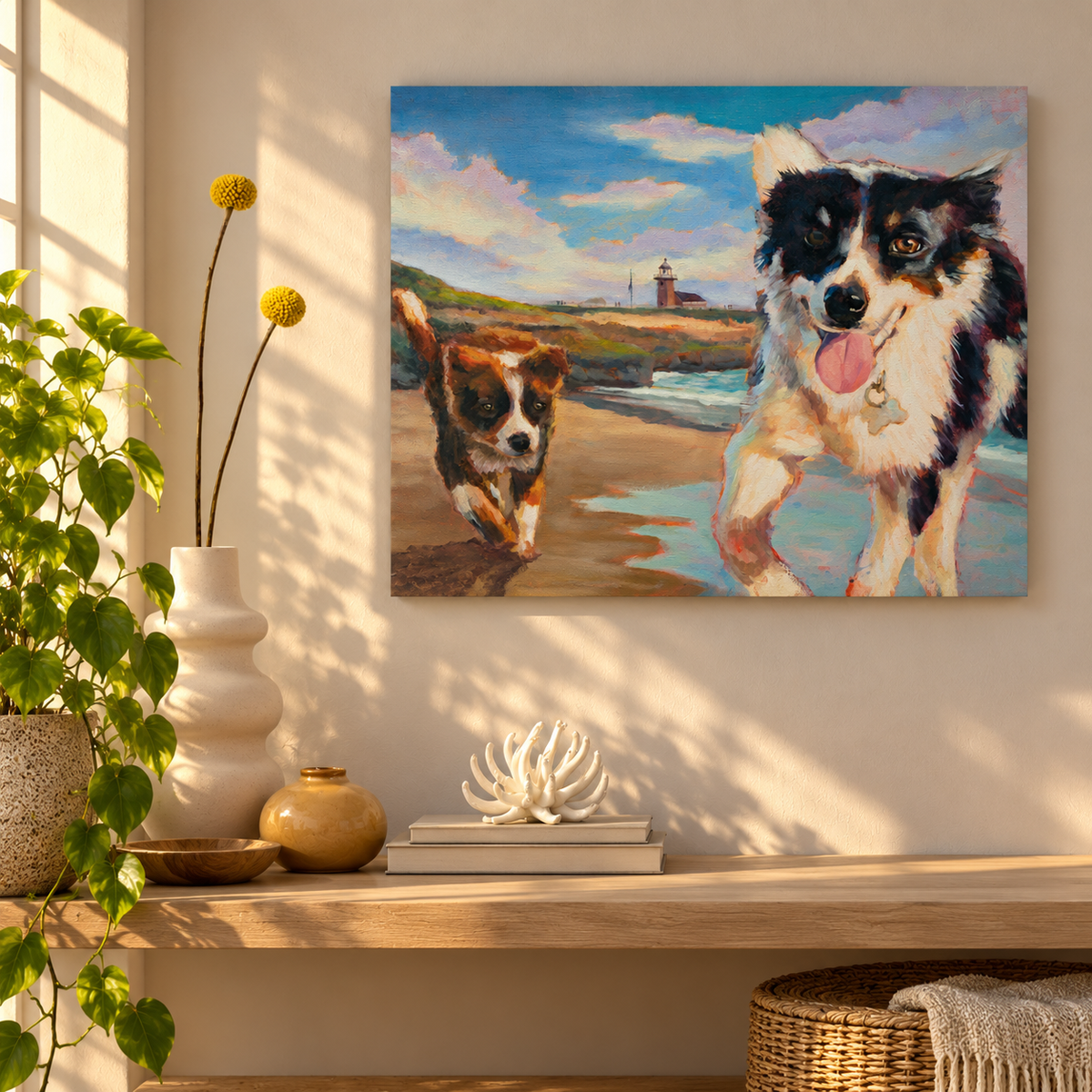Colorful coastal oil painting by Martina Goulart featuring two playful dogs running along a Santa Cruz beach with a lighthouse in the background, displayed in a cozy, sunlit room with warm neutral decor and green plants.