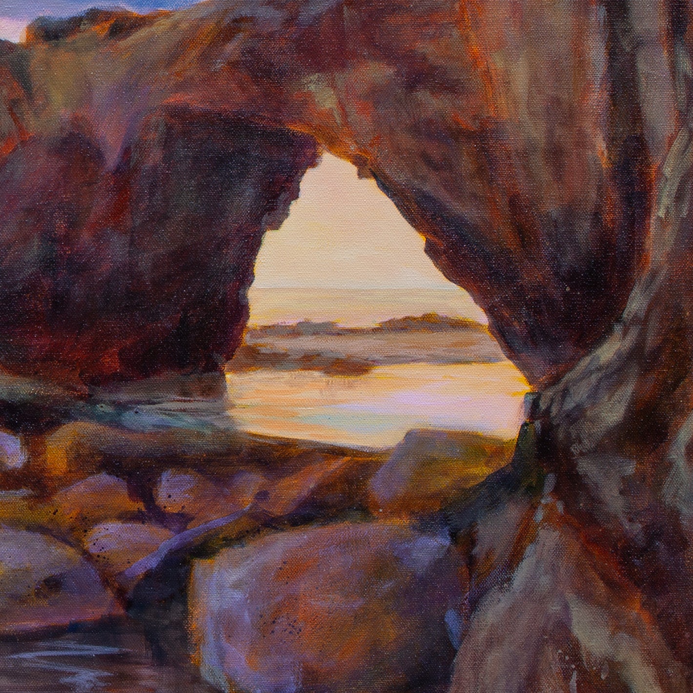 Close-up of red-brown rock arch with boulders in front and glowing orange sky and water reflections visible through the opening, from The Duck, the Dog, and the Sea.