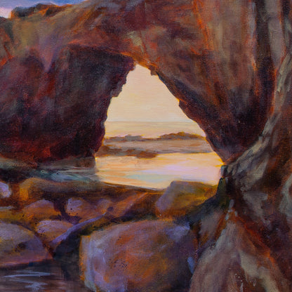 Close-up of red-brown rock arch with boulders in front and glowing orange sky and water reflections visible through the opening, from The Duck, the Dog, and the Sea.