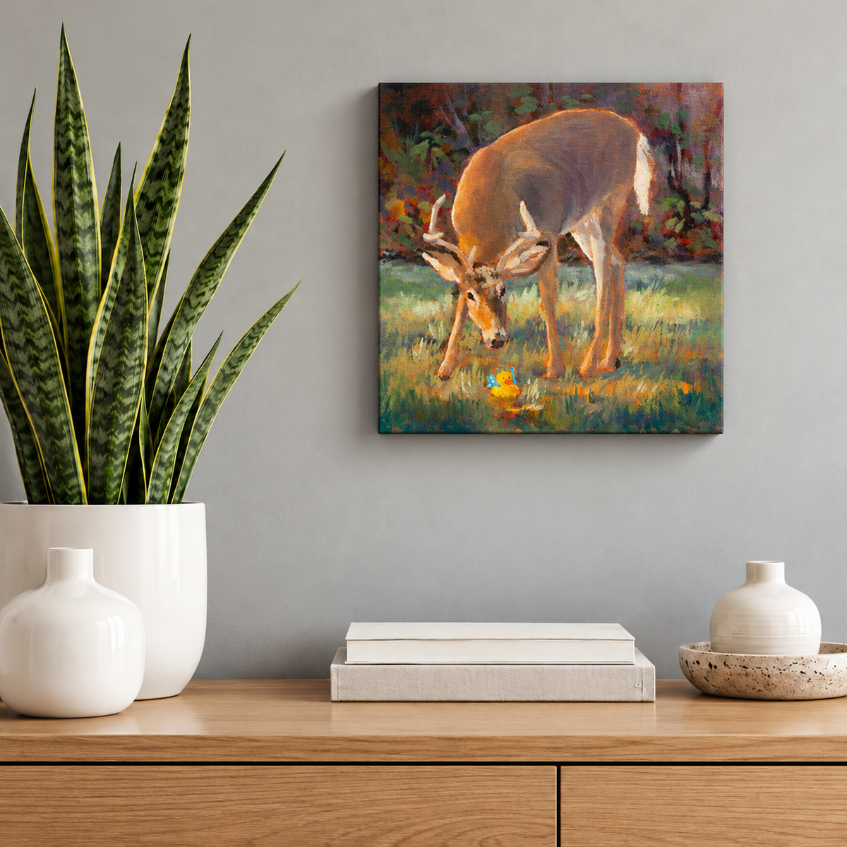 Small square deer oil painting by Martina Goulart featuring a curious buck and yellow rubber duck, displayed above a wooden cabinet with a snake plant and minimalist decor.