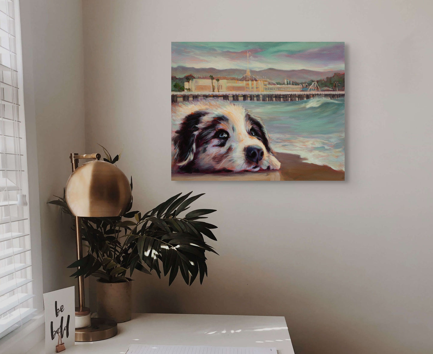Original painting of a dog by the Santa Cruz Boardwalk displayed above a desk with a green houseplant, coastal fine art by Martina Goulart.