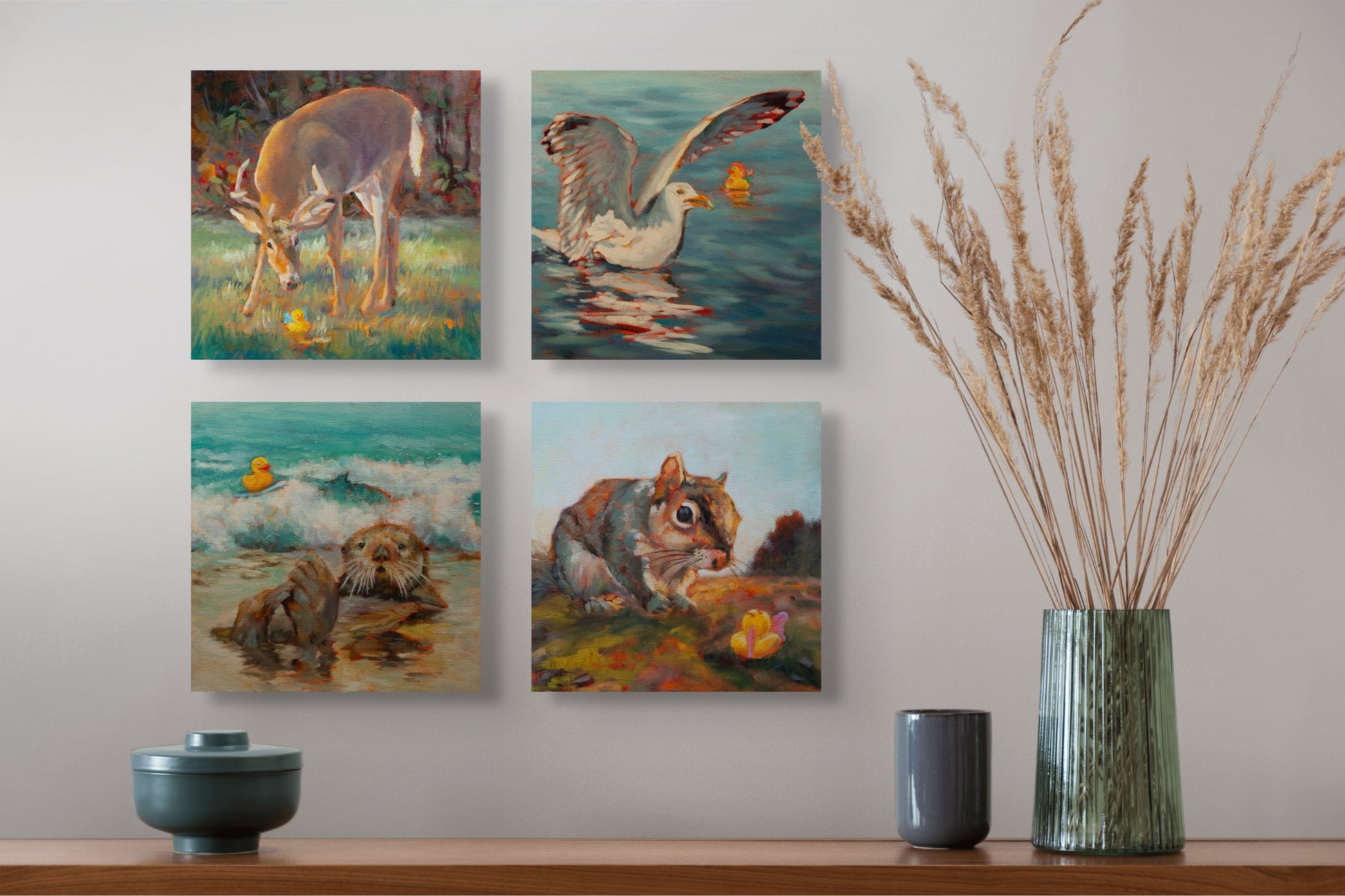 Four Wild Neighbors paintings — deer, seagull, otter, and squirrel — hanging above a brown table with a green vase, yellow grass, and two gray cups.