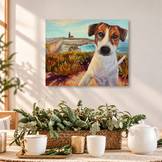 Colorful oil painting of a brown-and-white terrier overlooking the Santa Cruz coastline and lighthouse, displayed above a wooden dining table in a warm, sunlit home with natural greenery, woven textures, and cozy neutral decor.