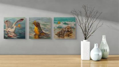 Three Wild Neighbors paintings — seal, otter, and seagull — hanging above a side table with three white vases and a twig, art by Martina Goulart.”