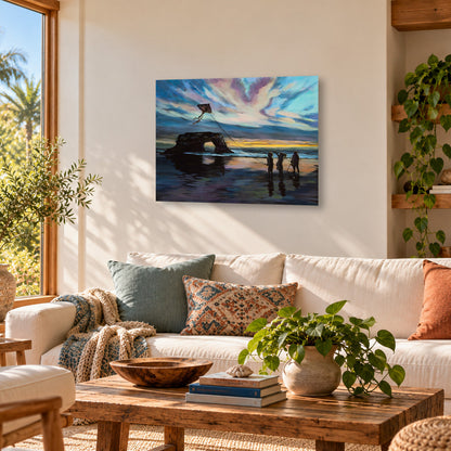 Colorful fine art print of three children flying a kite at Natural Bridges State Beach in Santa Cruz, California, featuring the iconic rock arch and dramatic sunset sky, displayed in a wooden frame above a cream sofa in a warm, sunlit coastal living room with natural wood furniture and inviting decor.