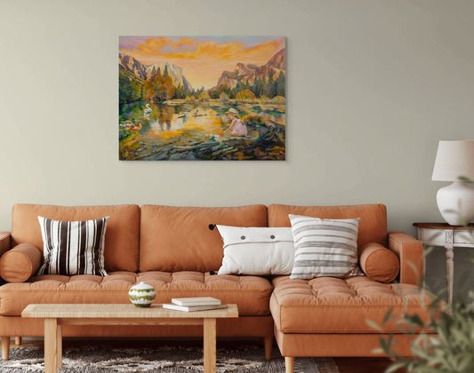 Painting The Peace of Play hanging above a brown couch with white pillows and lamp on side table in a cozy living room with warm, natural tones.
