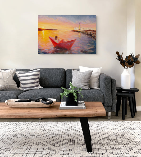 Living room with a gray sofa and wooden coffee table, featuring an original painting of a red boat at sunset with a lighthouse and paper boat entering Santa Cruz Harbor.