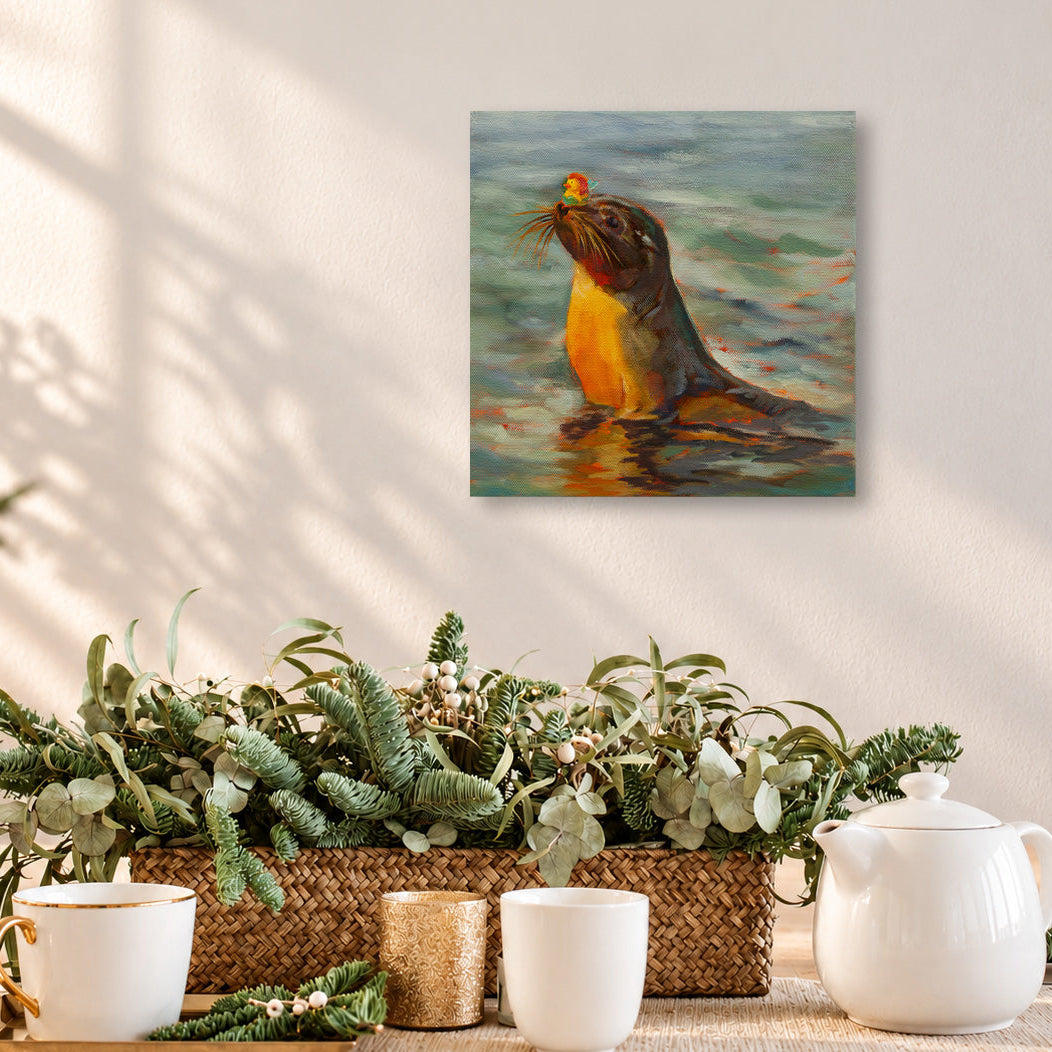 Colorful oil painting of a playful sea lion holding a small orange flower in its mouth while swimming in the ocean, displayed above a wooden dining table in a warm, sunlit coastal home with natural greenery, woven textures, and soft neutral decor.