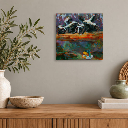 10x10-inch wildlife painting of playful skunks and a yellow rubber duck from Martina Goulart Studio’s Wild Neighbors series, displayed above a wooden cabinet with a snake plant and minimalist white decor.