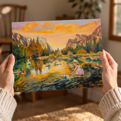Hands holding a Yosemite Valley print of a girl playing with paper boats during yellow and orange sunset. 