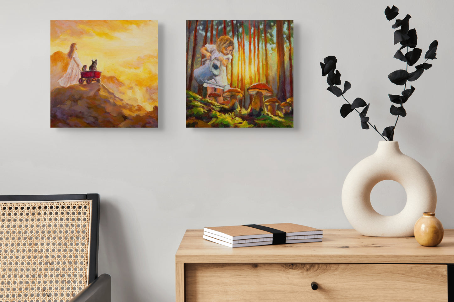 Two square paintings displayed side by side: one of a girl with a red wagon at sunrise, the other of a girl exploring mushrooms in a sunlit forest.