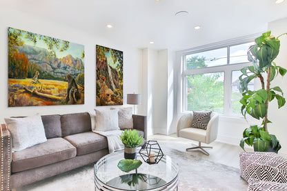 Modern living room with a gray sofa and large windows, featuring original fine art paintings from Yosemite Valley in warm yellow and orange tones.