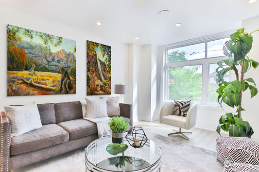 Modern living room with a gray sofa and large windows, featuring original fine art paintings from Yosemite Valley in warm yellow and orange tones.